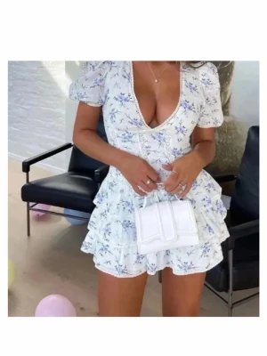 Vit blommig kortklänning med volanger Zara - Supersöt vit kortklänning med blått blommönster, djup v-ringning och puffärmar. Klänningen har flera volanglager i kjolen och markerad midja för en feminin siluett. Perfekt för varma dagar och somriga tillfällen. Från Zara. Kollar intresset. Köpte den för 990kr här på plick.