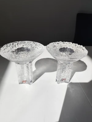 Isljus ljusstakar från Orrefors  - Två stycken isliknande ljusstakar från Orrefors i klart glas. Ljusstakarna har en rå, kristalliknande yta och bred öppning upptill. Perfekta som dekorativa detaljer i hemmet.