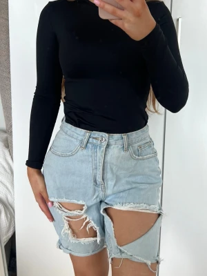 Shorts - Säljer ett par ljusblå jeansshorts med hög midja och stora slitningar framtill. Shortsen har råa kanter och klassisk knappgylf. Perfekta för en avslappnad och trendig sommarlook. Storlek 36 från Missguided 🩵