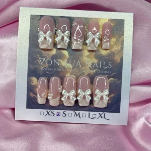 SilkPearl (S); Medium Square  - Superfina handgjorda press-on naglar i nude och pärlemor med 3D-rosetter i pärlvit och vita pärlor detaljer. Naglarna har en fyrkantig form och är dekorerade med handmålade french och hjärtan. Perfekt för dig som vill ha en söt och trendig look.S: 15 mm, 11,5 mm, 12 mm, 11 mm, 9 mm 