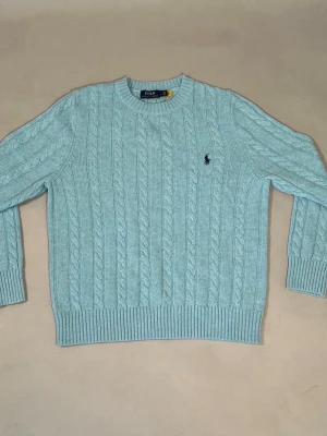 Ralph Lauren knit - Fin cable knit från Ralph Lauren som är i väldigt fint skick då den är i princip ny. Storleken är L. Fin ljusblå färg och perfekt att matcha med en skjorta eller bara t-shirt under, vilket är perfekt nu till våren och sommaren. Tag fås med och skickar beställnigen senast nästa dag (om den köps innan klockan 22). Bara att skriva vid minsta lilla fråga!