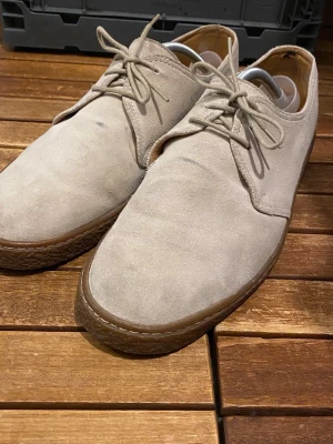 Beige mockaloafers från Wildbør - Snygga beige loafers i mocka från Wildbør med klassisk design och bruna gummisulor. Skorna har rundad tå, diskreta sömmar och matchande beige snörning. Perfekta för en clean och stilren look.