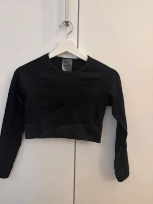 Svart ribbad croppad topp Aim'n - Svart croppad långärmad topp från Aim'n med ribbad struktur. Toppen har rund halsringning och sitter tight mot kroppen, perfekt för en sportig och trendig look.