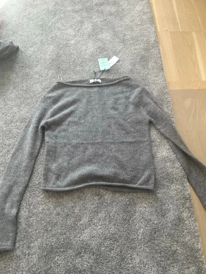 Grå stickad tröja Gina Tricot - Mysig grå stickad tröja från Gina Tricot i ullblandning. Tröjan har långa ärmar, rak passform och en enkel, stilren design som passar perfekt till jeans eller kjol. Materialet är mjukt och värmande, perfekt för kyligare dagar.