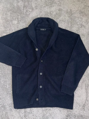 French connection cardigan - Mysig mörkblå stickad kofta från H&M med stora knappar framtill och bred krage. Koftan har långa ärmar, ribbade muddar och två fickor framtill. Perfekt för lager-på-lager och chill vardagsstil.