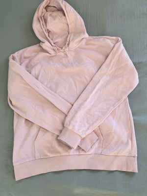 Ljusrosa hoodie med huva - En stilren ljusrosa hoodie med klassisk huva och känguruficka framtill. Hoodien har ribbade muddar vid ärmslut och nederkant. Perfekt för en avslappnad och trendig look. Materialet känns mjukt och bekvämt mot huden.