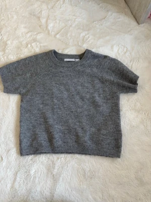Grå stickad tröja från 157 - Kortärmad stickad tröja i mjuk grå ullmix från 157. Tröjan har rund halsringning och ribbade kanter vid ärmslut och nederkant. Enkel och stilren design som passar perfekt till lager på lager. Knappt använd, pris kan diskuteras.