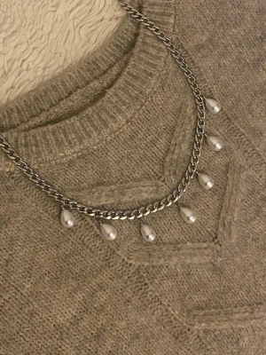 Silverfärgat halsband med pärlor - Ett snyggt halsband med silverfärgad rostfritt kedja och droppformade vita pärlor som hänger längs kedjan. Kedjan har en klassisk länkkonstruktion och pärlorna ger ett elegant och trendigt uttryck. Perfekt för dig som vill ha något stilrent med en twist.