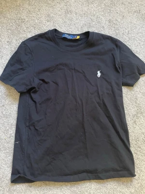 T-shirt Ralph Lauren - Klassisk svart t-shirt från Polo Ralph Lauren med broderad vit logga på bröstet. T-shirten har rund halsringning och korta ärmar. Perfekt basic-plagg med stilren design och skön passform i mjuk bomull.