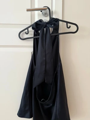 Svart halterneck topp - Snygg, svart halterneck topp med breda band som knyts i nacken. Toppens material är glansigt och faller superfint!