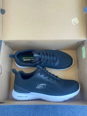 Svarta Skechers skor ge mig ett bra bud :)  - Snygga svarta sneakers från Skechers med vit sula och memory foam för extra komfort. Skorna har mesh-överdel, klassiska snörningar och Skechers-logga på sidan. Perfekta för dig som vill ha både stil och bekvämlighet i vardagen.