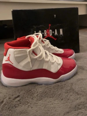 Air Jordan 11 Retro Cherry  - Säljer ett par Air Jordan 11 Retro Cherry med vit mesh och röd lackad läderdetalj. Skorna har högt skaft, genomskinlig sula och klassisk Jumpman-logga på sidan. Perfekta för dig som vill sticka ut med en ikonisk sneaker i rött och vitt.