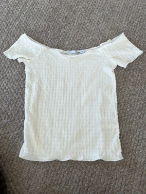 Offshoulder ribbad topp i ljus beige - Säljer en ljus beige offshoulder topp från Bik Bok med ribbad struktur. Toppen är kortärmad och har en slim passform som framhäver axlarna. Perfekt för dig som gillar en enkel och stilren look. Aldrig använd 
