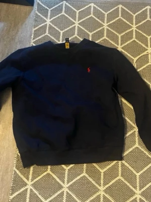 Mörkblå sweatshirt från polo ramp lauren - En enkel och stilren mörkblå sweatshirt med rund hals och långa ärmar. Tröjan har ribbade muddar vid ärmslut och nederkant. Perfekt för en avslappnad och casual look. Inget tryck eller logga syns på baksidan.