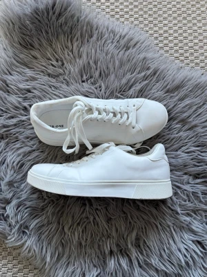 Vita låga sneakers - Stilrena vita sneakers med klassisk låg profil och vita skosnören. Skorna har en slät ovandel i syntetmaterial och en vit gummisula. Perfekta för dig som gillar minimalistisk och clean stil. Använda 1 gång!