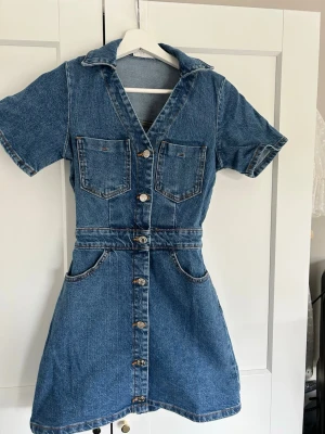 Kort jeansklänning med knappar - Snygg kort figursydd jeansklänning med v-ringning, korta ärmar och knappar framtill. Helt oanvänd, säljer då den är förliten💓