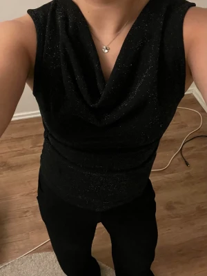 Glittrig festtopp - Svart topp med vattenfallsurringning. Har använts 1 gång. Väldigt bekvämt material. Den är i storlek S