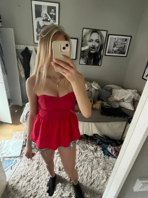 Röd axelbandslös topp med volang - Snygg röd axelbandslös topp med volang nedtill. Toppen har en bandeauformad överdel och sitter tight upptill ❤️