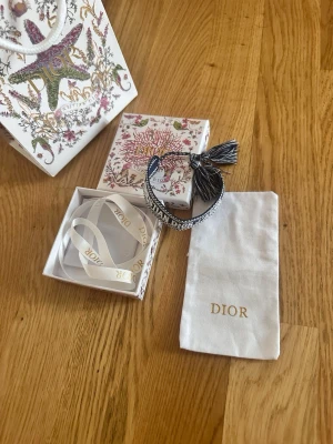 Dior J'Adior vävt armband - Snyggt vävt armband från Dior i svart och vitt med texten 'CHRISTIAN DIOR J'ADIOR'. Armbandet har justerbar knytning med tofsar i ändarna och levereras med originalpåse och ask. Perfekt accessoar för att lyfta din outfit.
