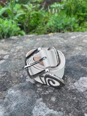 Vitt stussy bälte - Snyggt vitt bälte från Stussy med unik silverspänne och cool detalj i metall. Bältet är i slätt skinn och har en klassisk design som passar till många outfits. Perfekt accessoar för att lyfta din stil.