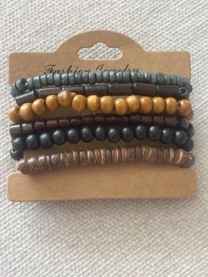 Set med 6 färgglada pärlarmband - Säljer ett set med fem armband i olika färger och former. Armbanden är gjorda av träpärlor i nyanser av brunt, svart, gult och grått. De har både runda och cylinderformade pärlor och passar perfekt för en avslappnad och trendig stil.