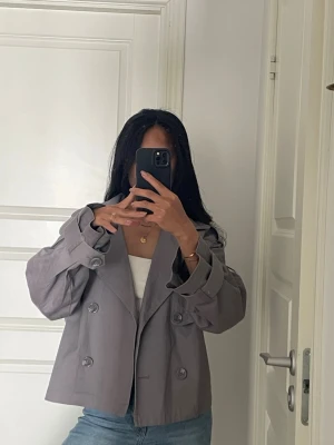Kort grå trenchcoat  - Storlek M. Liten fläck/prick på ärmen (se bild) 