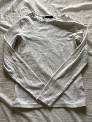 Vit långärmad topp från Lager 157 - En enkel och stilren vit långärmad topp från Lager 157. Tillverkad i mjuk bomull med rund halsringning och normal passform. Perfekt att matcha med jeans eller kjol för en clean look.