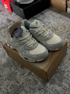 Asics gråvita sneakers mesh - Snygga sneakers från Asics i grått och vitt med mesh- och mockadetaljer. Skorna har en chunky sula och klassisk Asics-logga på sidan. Lätta att matcha och perfekta för en sportig look. Skön passform och ventilerande material.