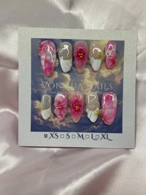 Camellia (XS);Medium Almond - Handgjorda press-on naglar i en medium lång mandelform. Naglarna har en mix av rosa och vita nyanser med marmorerad effekt, dekorerade med små 3D-blommor i rosa och guldiga detaljer. Perfekt för dig som vill ha en unik och kreativ nageldesign.XS: 14 mm, 11 mm, 11,5 mm, 10 mm, 8 mm 