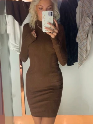 Brun ribbad klänning  - Säljer en brun ribbad långärmad klänning. Klänningen har en kroppsnära passform, hög hals och är tillverkad i ett stretchigt material som sitter snyggt på kroppen. Helt ny med prislapp kvar!