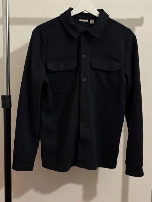 Blå Overshirt från Only&sons - Blå overshirt från med klassisk krage, knäppning framtill och två bröstfickor med lock och knapp. Använt lite grand men den har inga defekter och är i mycket bra skick. Står som xs men passar som s