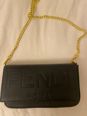 Svart Fendi handväska med guldkedja - Snygg svart handväska från Fendi. Har använt den en gång och inga skador 