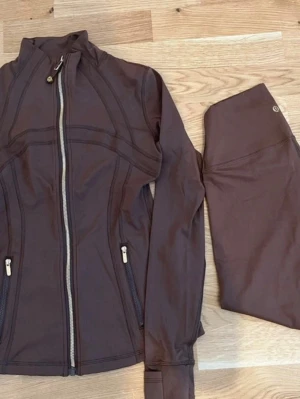 Lululemon Träningsset - tröja & leggings storlek 4 - Träningsset från Lululemon i storlek 4, passar XS-S. Träningströja och matchande leggings. Tröjan har dragkedja framtill och hög krage. Leggingsen är ankellånga med hög midja. Båda plaggen har Lululemons logotyp. Helt oanvända och redo för en ny användare.