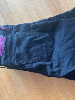 Svarta jeans från weekday - Säljer ett par svarta jeans från Weekday med utsvängda ben och klassisk femficksdesign. Jeansen har en cool lila patch med Monki-logga bak och är tillverkade i bomull med lite stretch. Perfekta för dig som gillar en avslappnad och trendig stil. Jeansen är andvända en gång. Skriv för fler bilder eller frågor!🥰