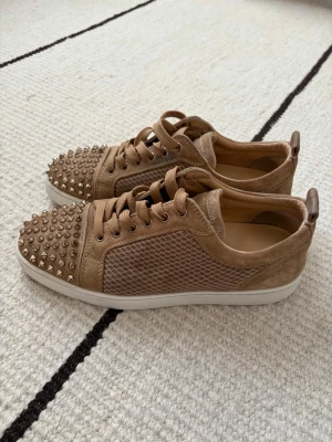 Beige Louboutin skor med nitar 41.5 - Selling authentic men's Christian Louboutin low-top sneakers in beige suede with silver spikes. Size 41 1/2, Fits also 42 / 42.5 They are in excellent, lightly worn condition. These are guaranteed 100% genuine. You can check the photos for all the authenticity details like the stamps, insoles, and the rea soles. I will ship out on the exact same day you buy them. Message me if you have any questions!