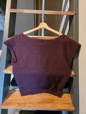 Vinröd stickad ärmlös tröja från Nelly - En vinröd stickad tröja med båt halsringning och ärmlös design. Tröjan har ribbad nederkant och är gjord i ett mjukt material som passar perfekt för lager-på-lager. Enkel och stilren look. Storlek M
