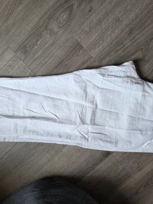 Vita vida linnebyxor från Gina - Säljer ett par vita linnebyxor med avslappnad passform och raka ben. Byxorna är tillverkade i ett lätt och luftigt linnetyg, perfekta för en chill och stilren look. Inga synliga detaljer eller mönster, bara clean och enkel design. Helt oanvända, strl L