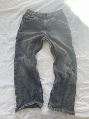 Svarta/gråa raka jeans med tvättad look - Säljer ett par svarta jeans med rak passform och snyggt tvättad vintage-look. Storleken är W26 (Eu storlek 34-36) 