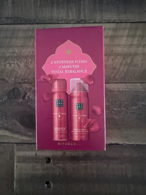 Rituals Ayurveda Icon Set - Säljer ett Rituals Ayurveda Icon Set med två produkter: en foaming shower gel och en body lotion mousse. Båda kommer i snygga röda flaskor på 50 ml vardera, förpackade i en elegant röd presentask med guldiga detaljer och rosenbladsmotiv.
