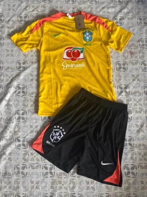 Brasilien fotbollskit Nike gul/svart - Brasilien fotbollsträningsset i storlek S. Shortsen har fickor med dragkedjor. Helt nya och oanvända, perfekt till sommaren. Hör gärna av vid frågor!