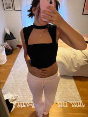 Svart croppad topp från Zara - Trendig svart croppad topp från Zara med hög hals och öppen detalj framtill. Toppen är ärmlös och har en slim passform som framhäver midjan. Perfekt att styla med höga byxor eller kjol för en cool look.