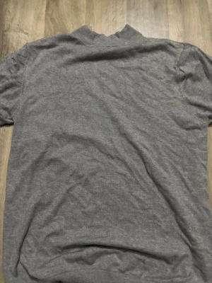 Grå polotopp från ZARA - Snygg grå polotopp från ZARA i mjukt material. Toppen har korta ärmar och en hög krage som ger en clean och stilren look. Perfekt att matcha med jeans eller kjol för en enkel men trendig outfit.