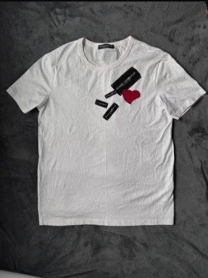 Vit Dolce & Gabbana t-shirt med hjärta - Vit t-shirt från Dolce & Gabbana med flera svarta broderade logolappar och ett rött hjärta på bröstet. Vintage som faaan. Sitter som M