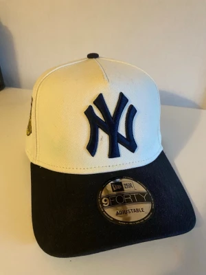 New Era Yankees keps vit och svart - Snygg New Era 9FORTY keps med New York Yankees-logga framtill. Kepsen är vit med svart böjd skärm och justerbar passform. Broderad logga i mörkblått och klassisk basebollstil. Perfekt accessoar för en sportig look.