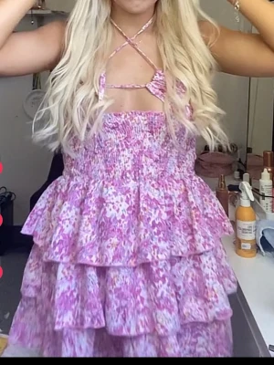 Rosa blommig volangklänning - Använd 1 gång!Supersöt kort klänning med rosa och vita blommor, volanger i flera lager och smockad överdel. Klänningen har smala axelband som korsas framtill och en unik cut-out detalj vid bysten. Perfekt för sommarens alla tillfällen!