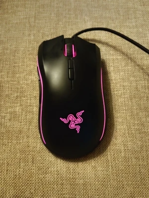 Razer Mamba Elite gamingmus svart/rosa - Gamingmus från Razer, modell Mamba Elite. Svart plast med rosa LED-belysning längs sidorna och loggan. Ergonomisk form med flera knappar och sladdanslutning. Perfekt för gaming och har upp till 16 000 DPI för exakt styrning.