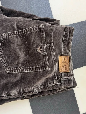 Bruna jeans från Armani Jeans - Säljer ett par bruna jeans från Armani Jeans med klassisk femficksmodell och AJ-logga på bakfickan. Jeansen har en snygg tvättad look och detaljer i metall. Perfekta för dig som gillar stilrena och tidlösa plagg.