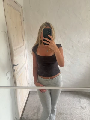 Brun ribbad topp med fyrkantig ringning - Snygg brun ribbad topp med korta ärmar och fyrkantig ringning. Toppens material är stretchigt och sitter tight mot kroppen, perfekt för en trendig och enkel look. Passar till både jeans och kjol för en stilren outfit.
