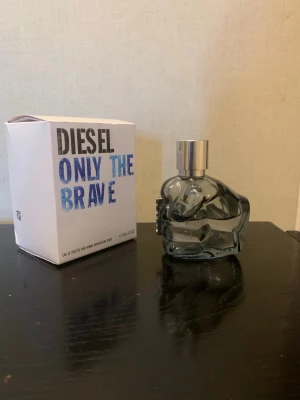 Diesel Only The Brave parfym - Diesel Only The Brave parfym med en unik flaska formad som en knytnäve i transparent gråblått glas och silverfärgad kork. Förpackningen är vit med blå och svarta detaljer. En cool och maskulin doft som sticker ut i badrumshyllan.