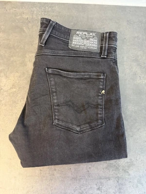 Svarta Replay Anbass jeans W34 L32 - Snygga svarta slim jeans från Replay med klassisk femficksdesign och diskret logga på bakfickan. Jeansen har en smal passform och är tillverkade i mjukt denimtyg som ger en bekväm känsla. Perfekta för en trendig och avslappnad stil.